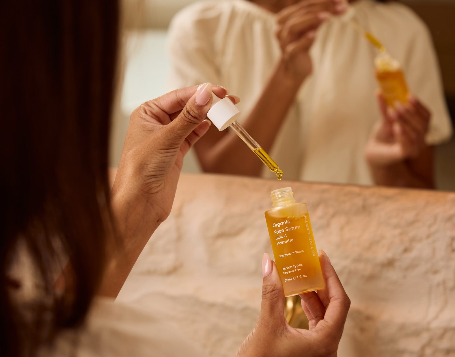 Woman applying Active Earth Organic Face Serum with a dropper at the mirror